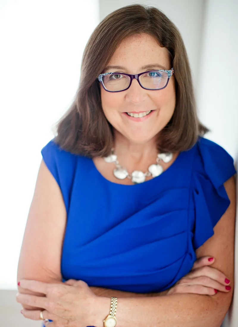 Debra Vey Voda-Hamilton - Debra Hamilton Debra Vey Voda-Hamilton smiles confidently while wearing a royal blue dress, glasses, and a statement necklace. - Debra Hamilton